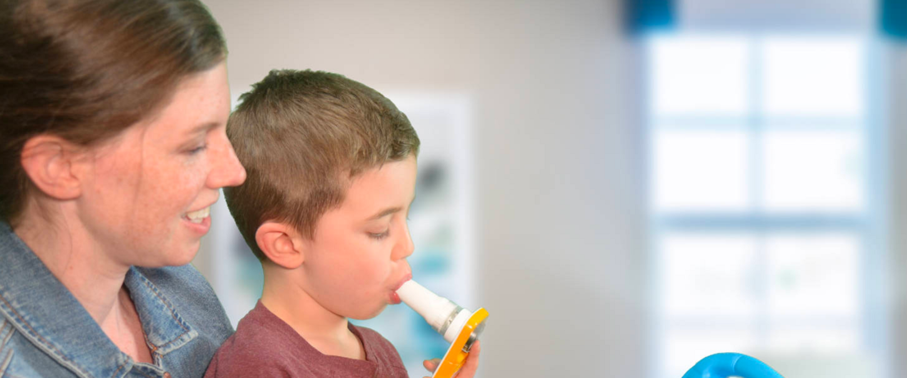 Mother holds son while he uses at home spirometer