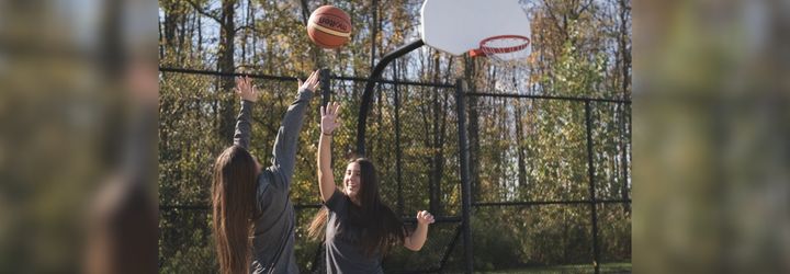 Deux filles jouant au basketball sur un terrain de basketball extérieur par une journée d'automne ensoleillée et entouré d'arbres.